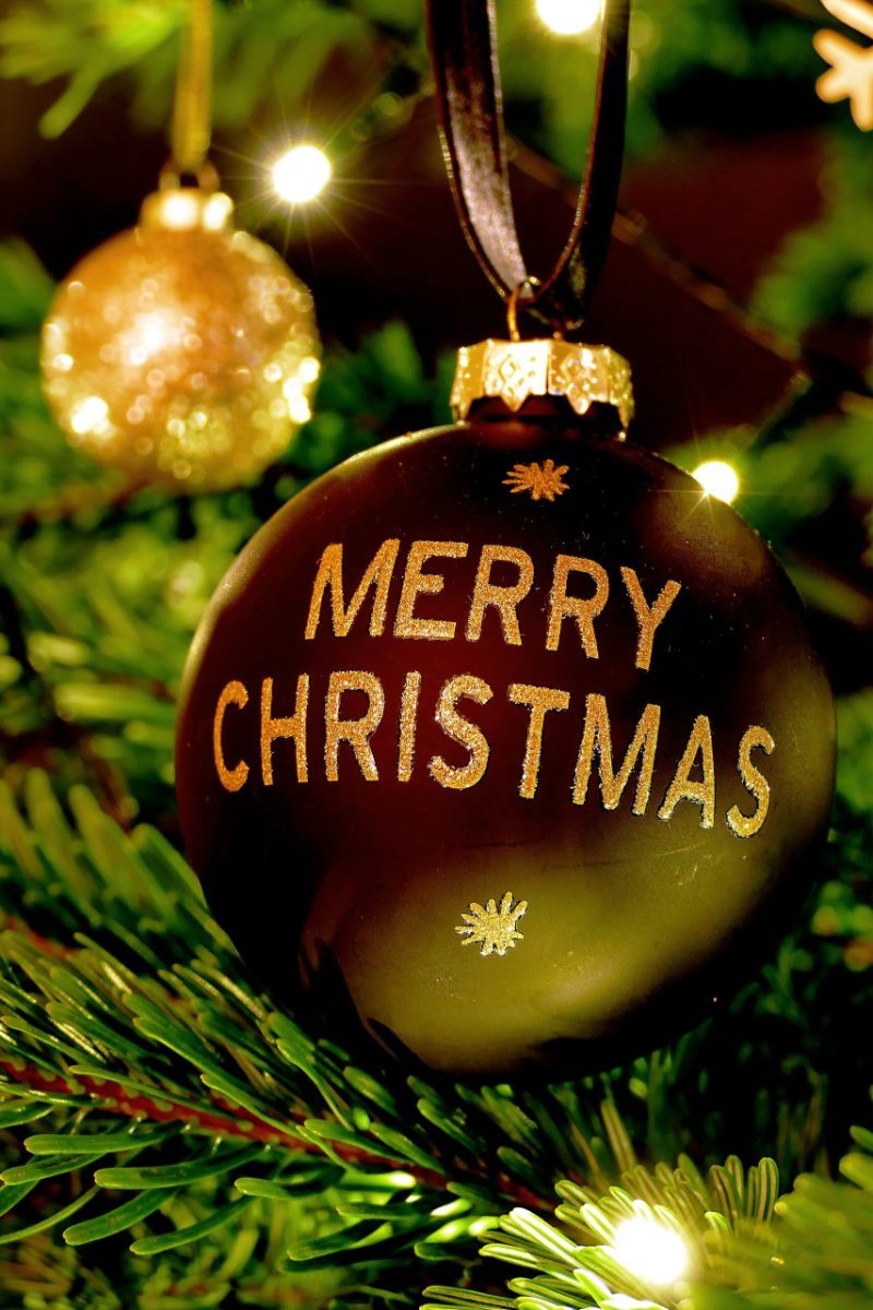 Christbaumkugel mit der Aufschrift Merry Christmas am geschmückten Tannenbaum